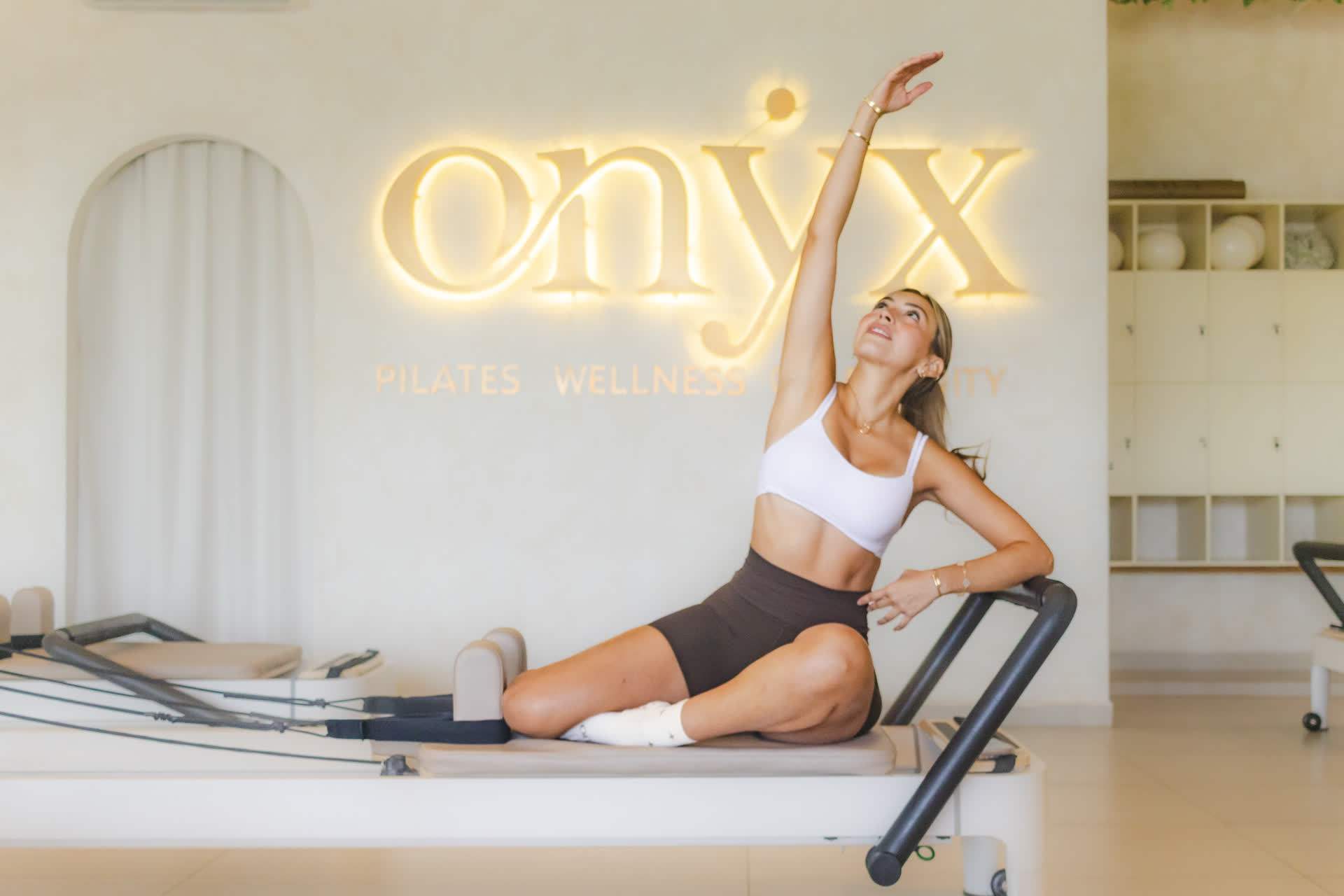 Alumna estirándose sobre el reformer bajo el letrero luminoso de Onyx