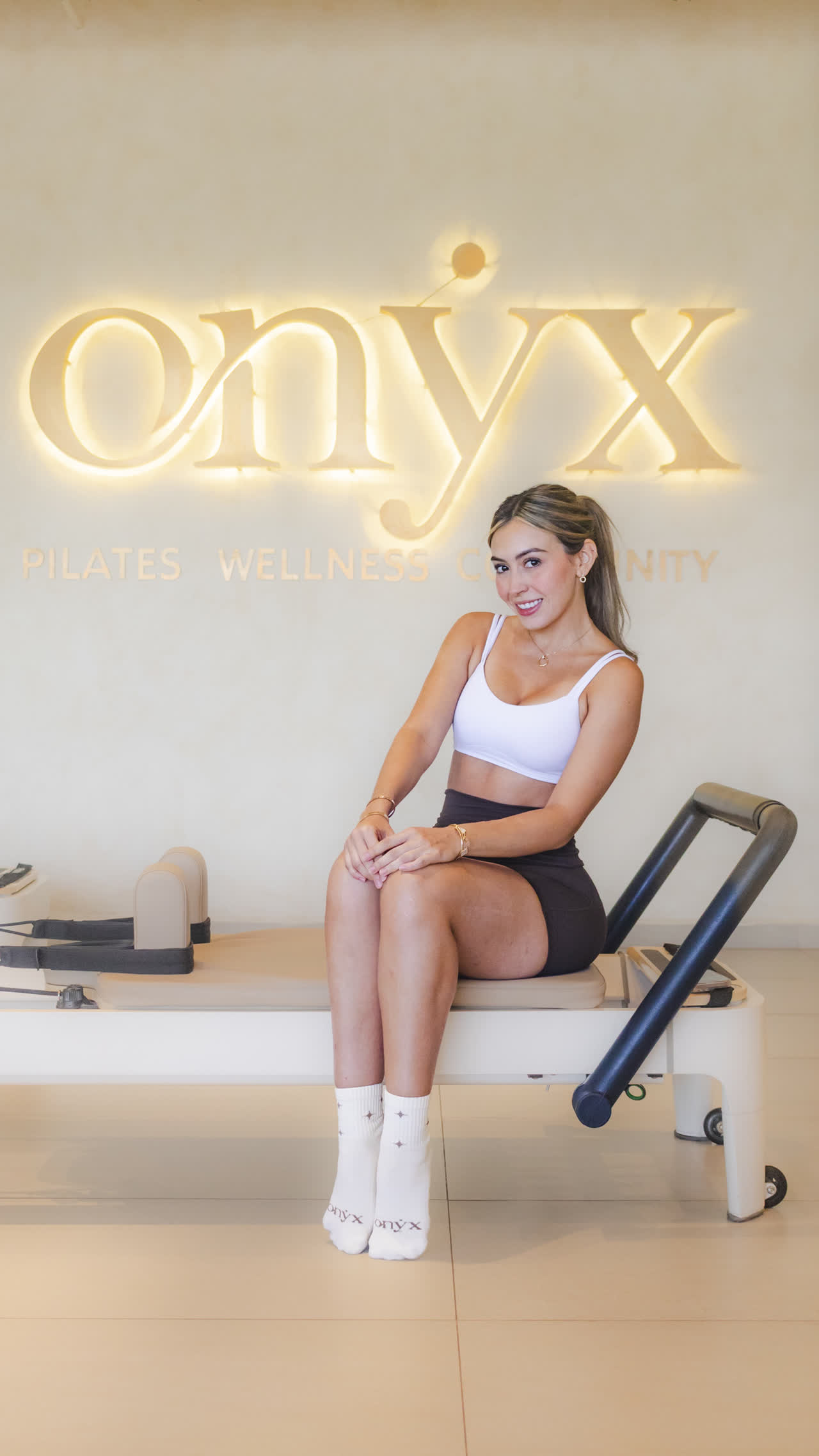 Alumna sentada en un reformer bajo el letrero luminoso de Onyx